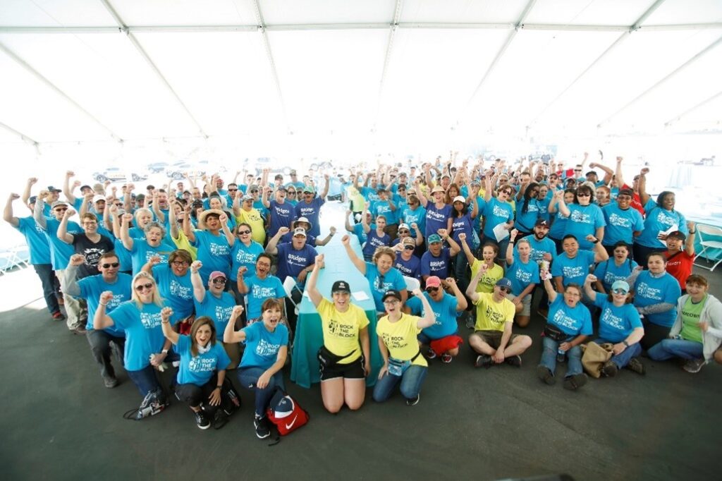A photo of many people with their firsts raised in the air. The people are volunteers with Habitat for Humanity and most of them are wearing branded Habitat for Humanity t-shirts.