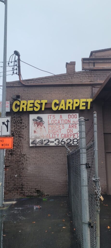 Exterior of the Crest Contract Carpets warehouse with a sign denoting that it's a "dog" location.