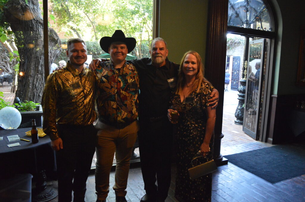 Four individuals, members of the Goodman family, pose for a photo at Crest Carpets anniversary event.