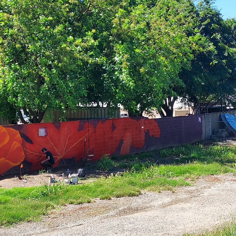 Artists working on a mural in Sacramento's River District. The mural is on a long wall and is a colorful depiction of wildflowers.